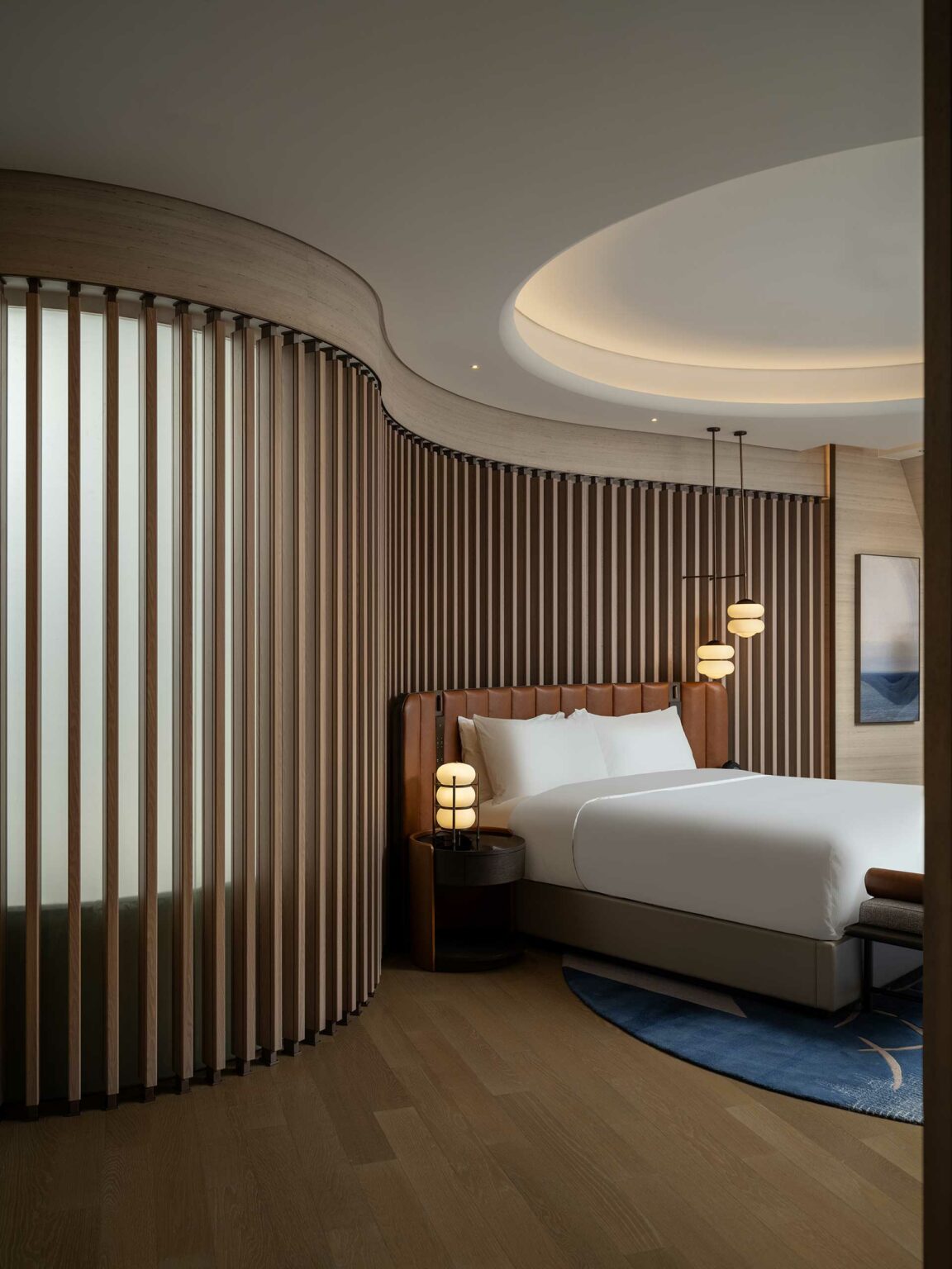 Modern hotel bedroom with curved wooden slats, a bed with white linens, and round pendant lights. A circular ceiling cutout adds elegance and warmth.