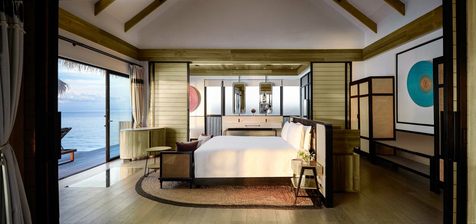Luxurious resort oceanfront bedroom with a large bed, wooden accents, and modern decor. Glass doors offer a sea view, creating a serene and relaxing atmosphere.