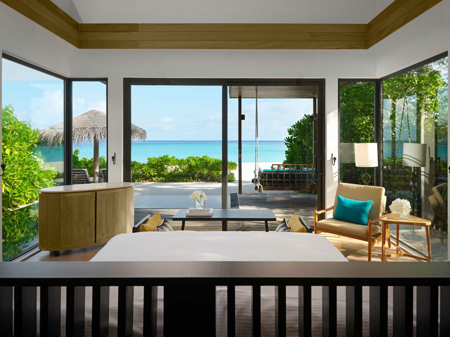 Luxurious resort beachfront room with large windows offering an ocean view. Features a comfortable bed, chic furniture, and tranquil, tropical ambiance.