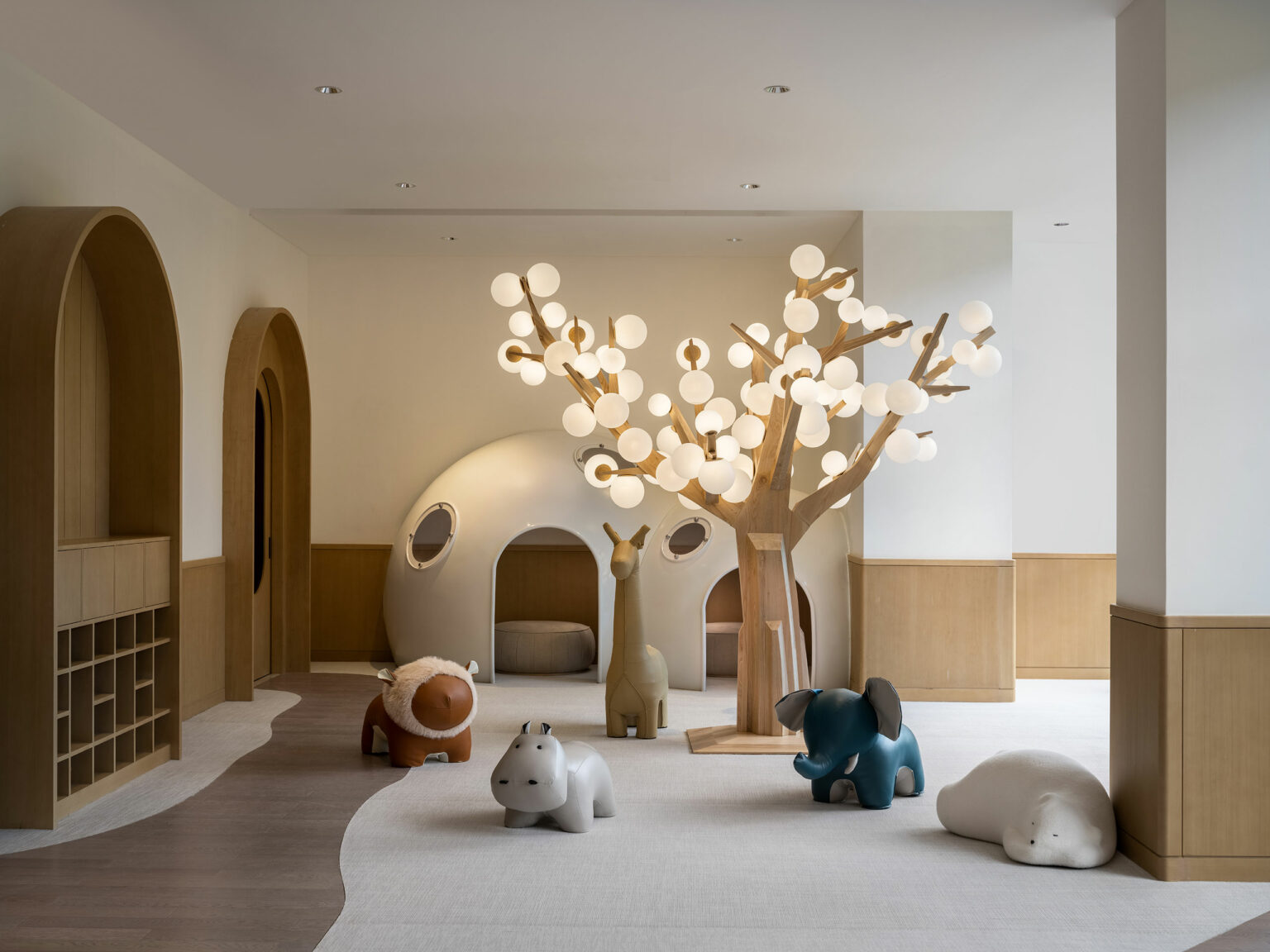 A serene hotel children's playroom featuring a whimsical wooden tree with glowing orbs, animal sculptures, and a cozy dome-shaped nook, conveying a playful ambiance.