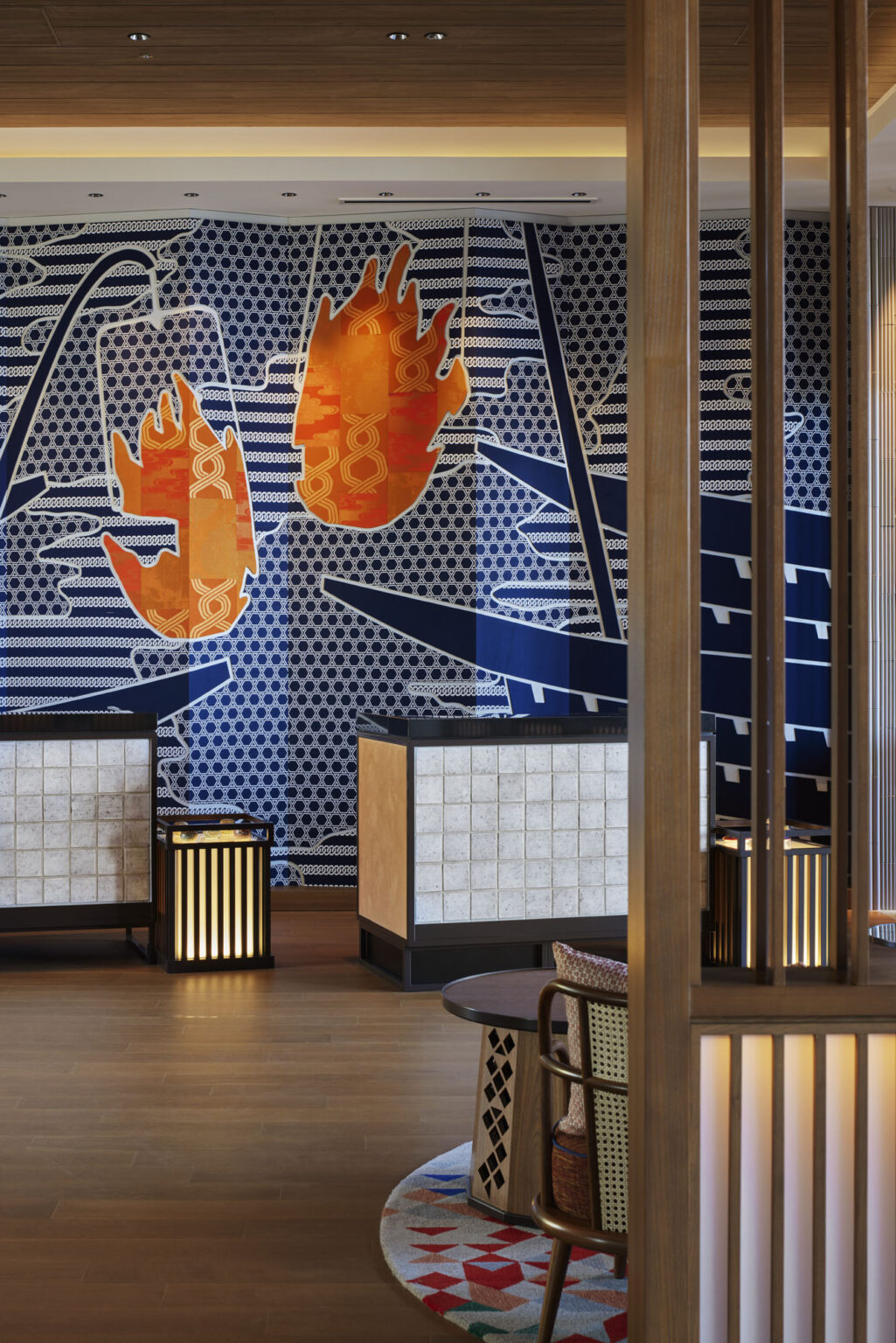 Hotel lobby interior featuring a bold blue-patterned wall with large, vibrant orange abstract shapes. Wood elements and soft lighting create a warm, welcoming tone.