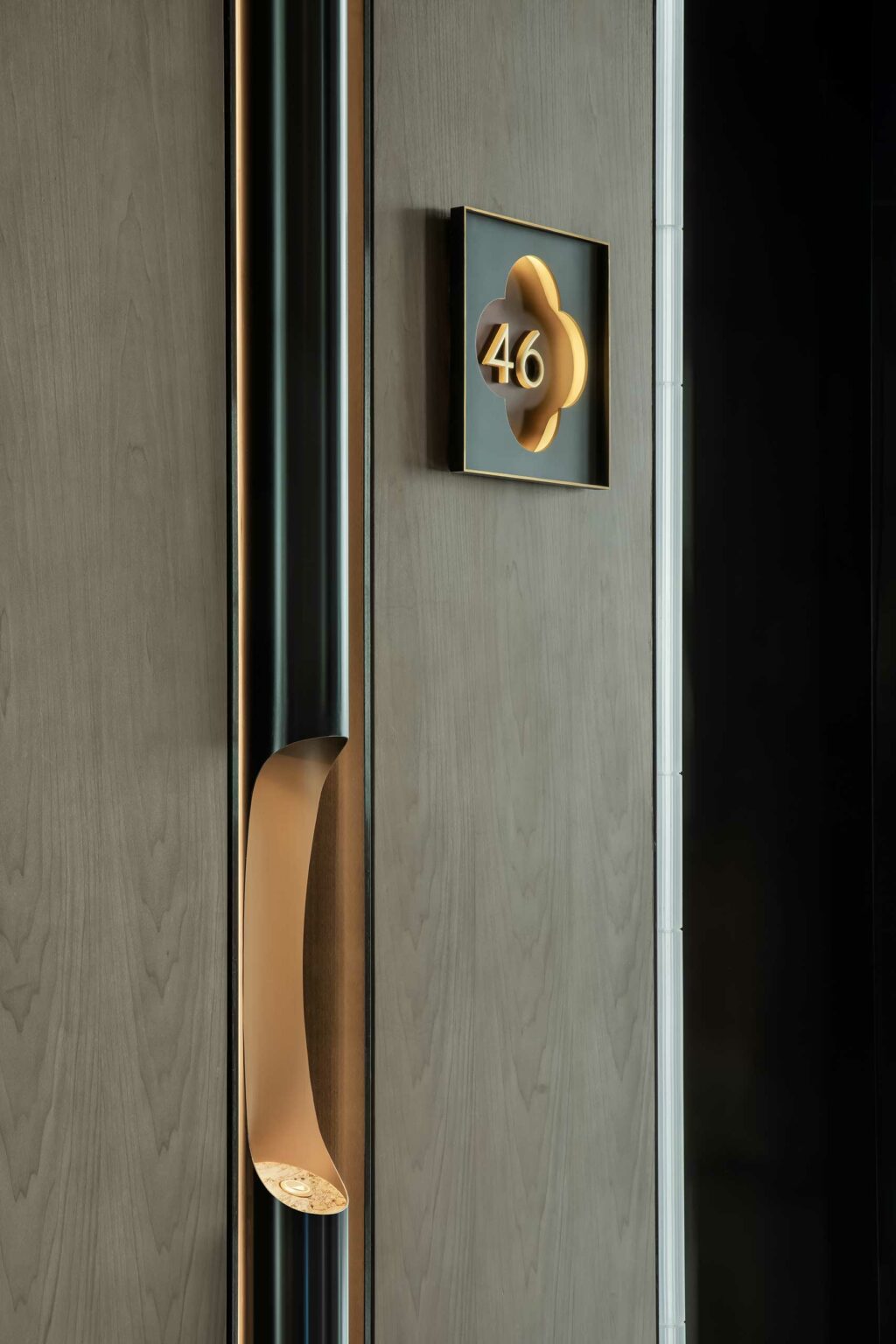 Modern hotel door with wood paneling and sleek metallic handle. A gold-accented room number 