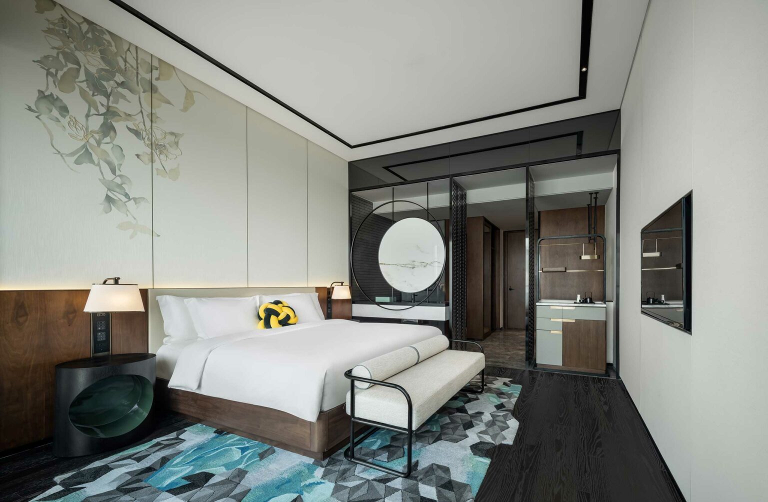 Modern hotel room with a large bed, elegant lighting, and abstract wall art. Features sleek furniture, a geometric rug, and a stylish ensuite bathroom. Calm ambiance.