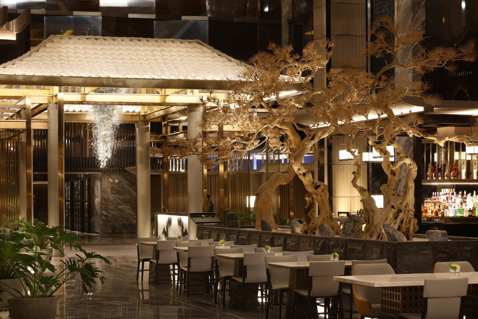 Luxurious hotel all day dining featuring elegant wooden sculptures, white-roofed pavilion, marble floors, stylish seating, and a chic bar, creating a sophisticated ambiance.