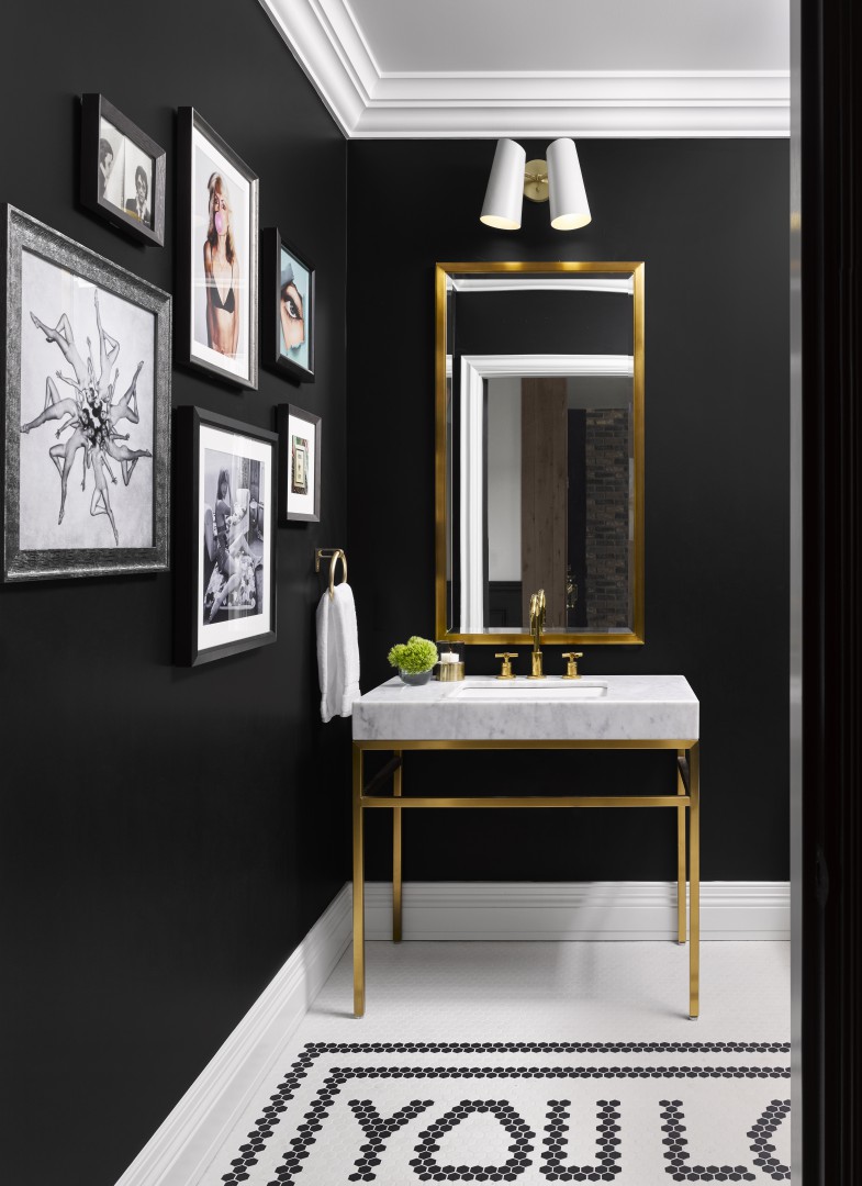 Elegant black and white suite bathroom with gold accents. Features a gallery wall of framed art, a marble sink with gold fixtures, and geometric tile flooring.