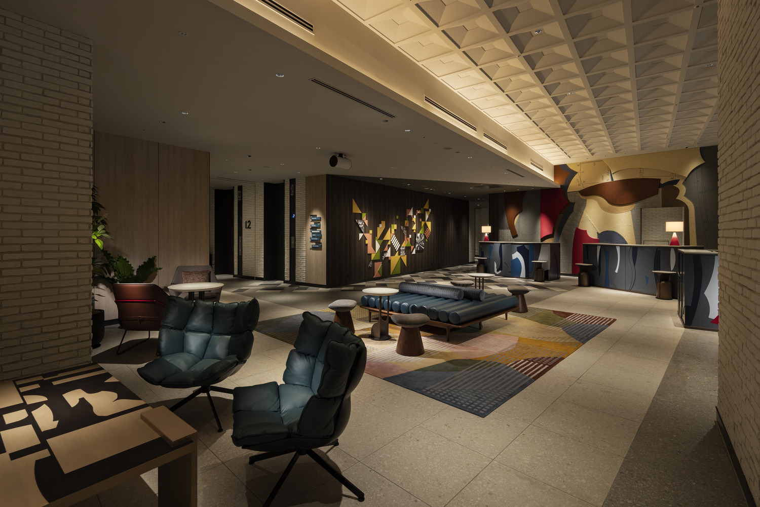 Modern hotel lobby featuring abstract wall art, geometric-patterned carpet, and stylish seating. Large windows reveal a cityscape at dusk, creating a sophisticated ambiance.