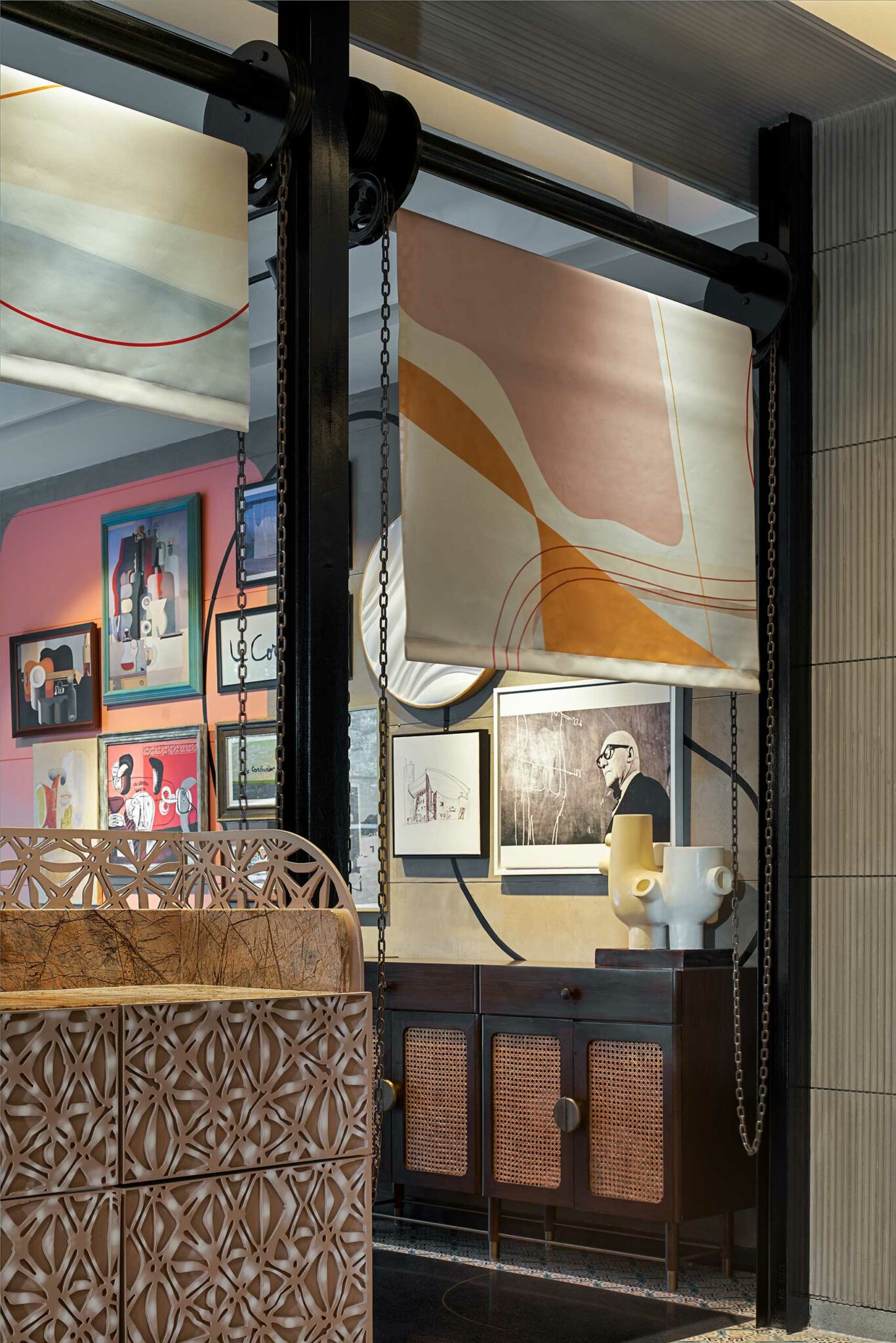 A stylish hotel interior with abstract geometric curtains, a modern sideboard with pottery, and a gallery wall featuring vibrant and monochrome art pieces.