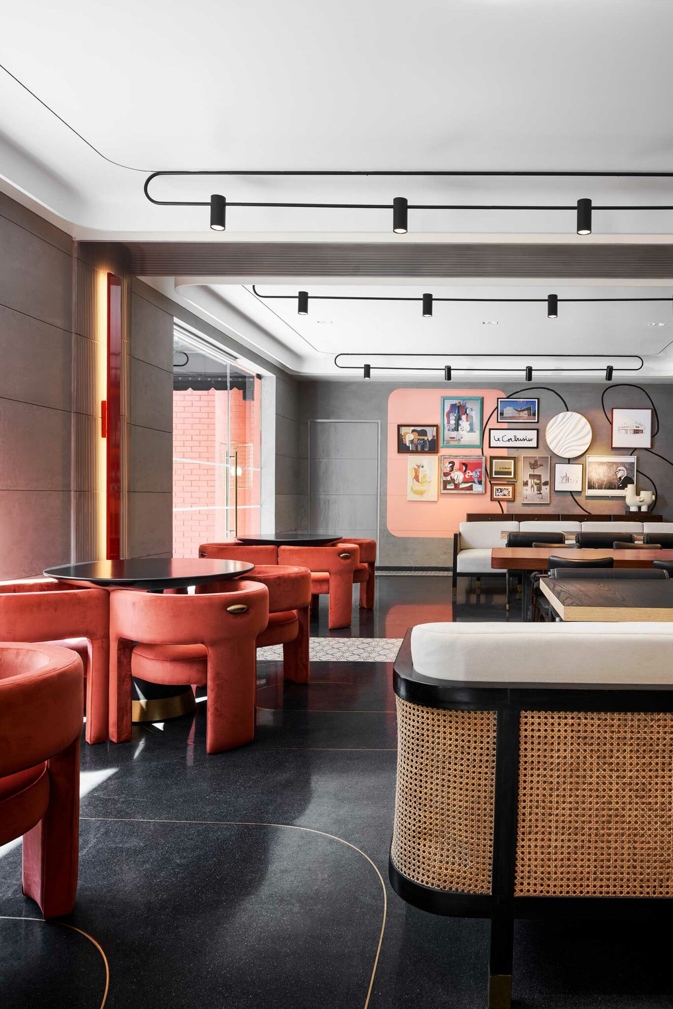 Modern hotel cafe area with sleek black tables, plush orange chairs, framed art on the walls, and warm lighting, creating a chic, cozy ambiance.