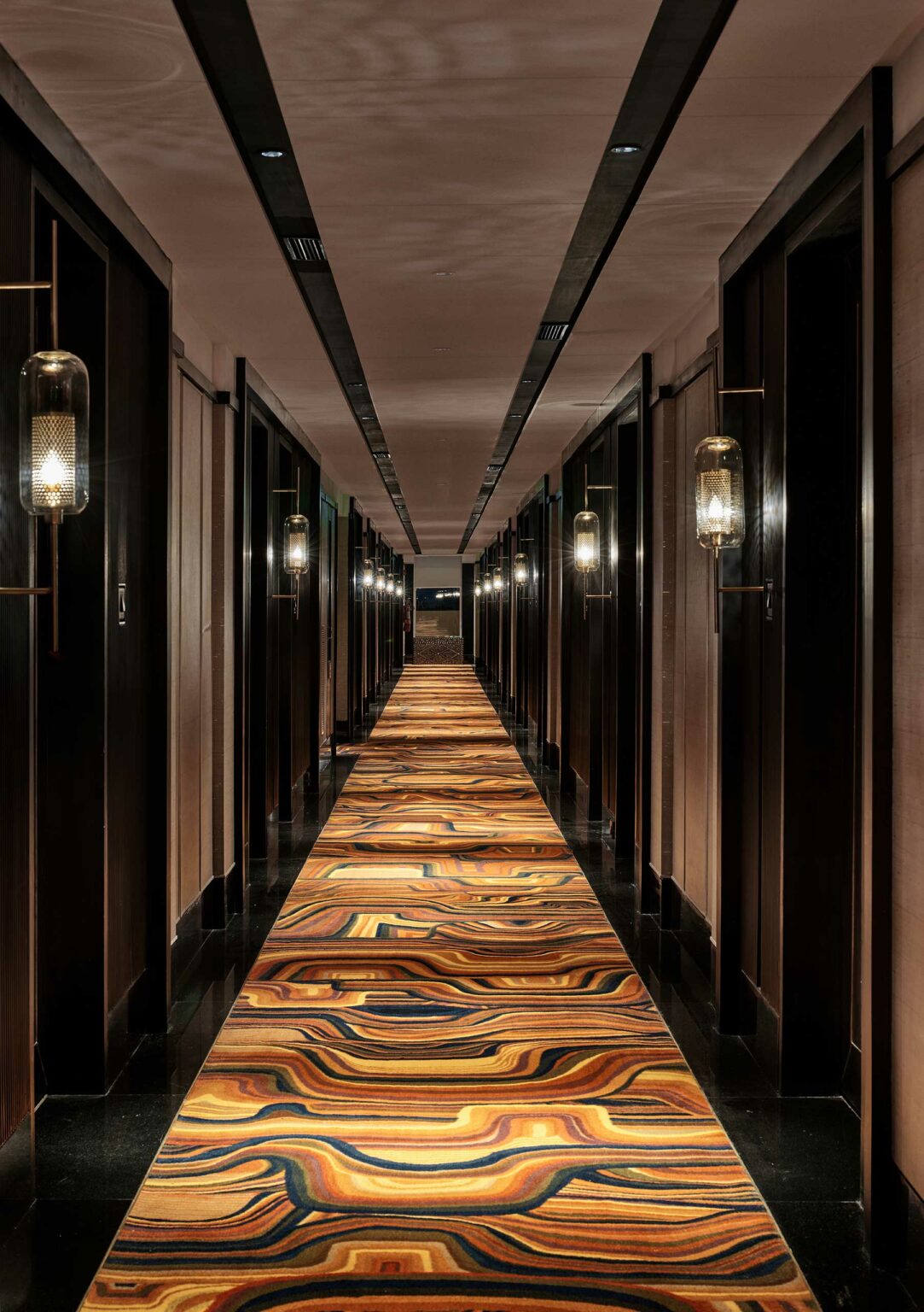 Dark wood hotel hallway featuring a vibrant, wavy-patterned carpet.