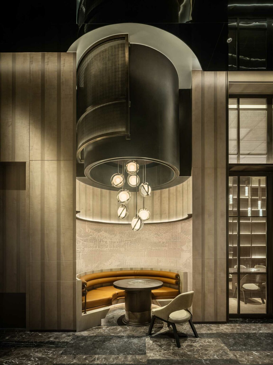 Elegant modern hotel lounge with circular seating and a round table, enclosed by wood paneling. A striking chandelier hangs above, illuminating the space warmly.