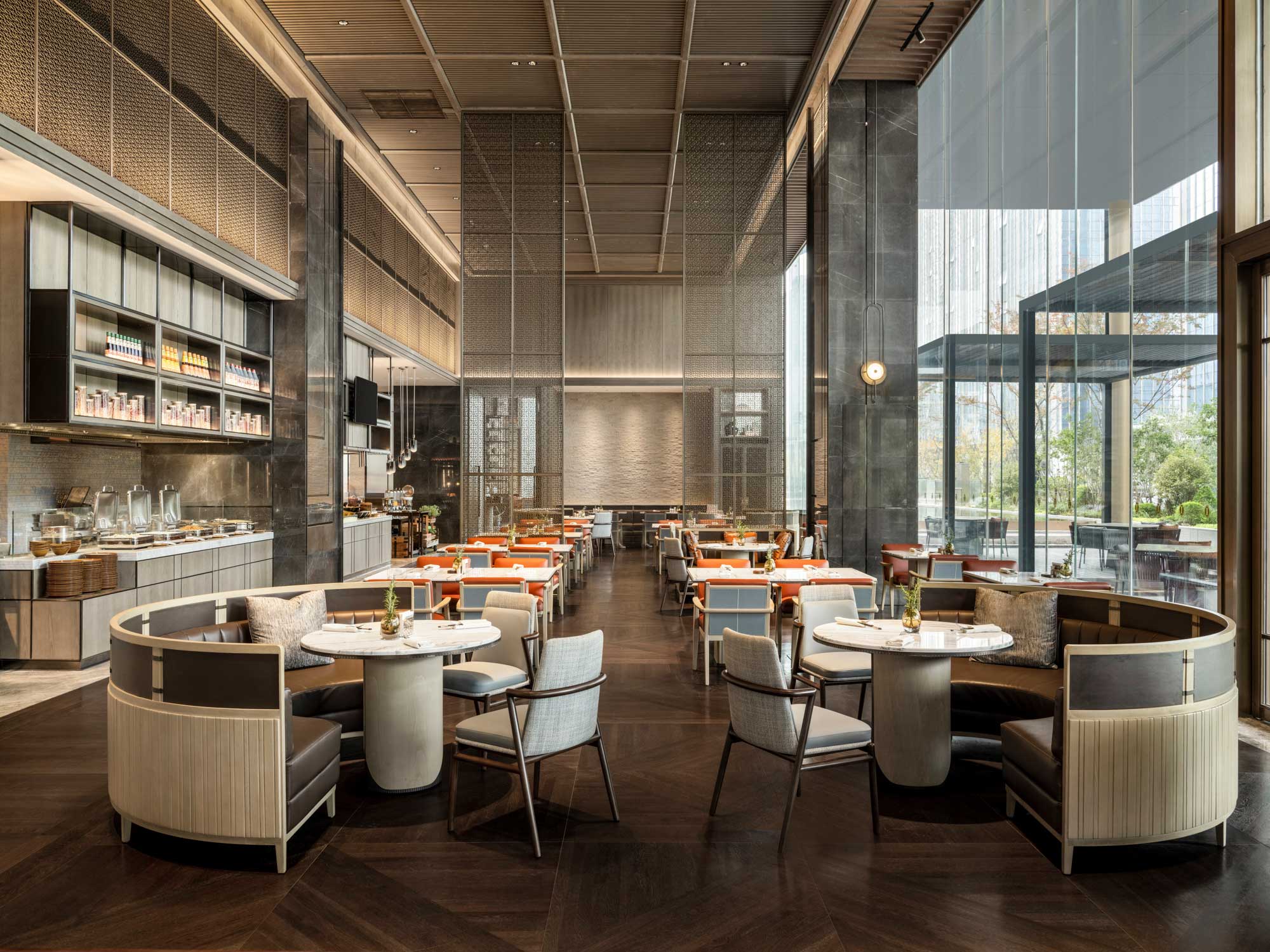 Spacious, elegant hotel all day dining with contemporary design, round tables, cushioned chairs, large windows providing natural light, and outside view.