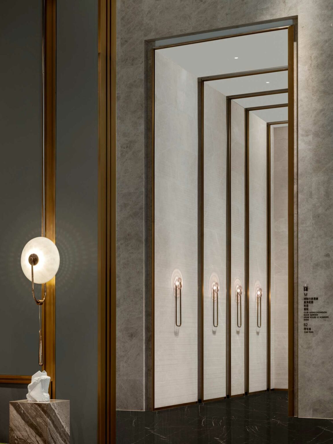 Elegant hotel interior features tall, narrow mirrors with bronze trim, reflecting a modern, ambient light fixture. The space conveys luxury and refinement.