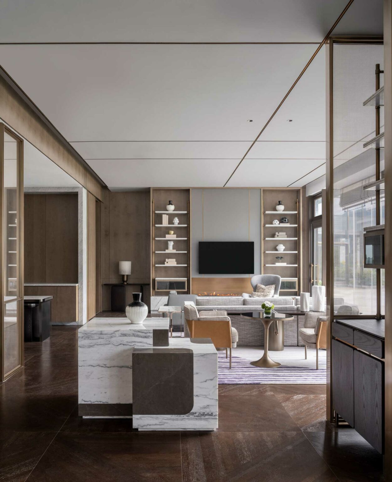 Modern hotel multi-purpose room with neutral tones featuring a marble island, built-in shelves, a wall-mounted TV, and plush seating. The space feels serene and elegant.