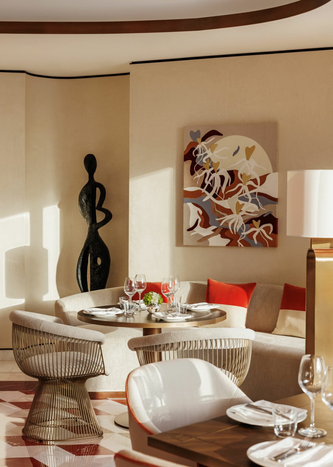 Elegant dining setup in a cozy corner of a luxury hotel with abstract art and a black sculpture. Soft lighting, red cushions, and modern chairs enhance warmth and sophistication.