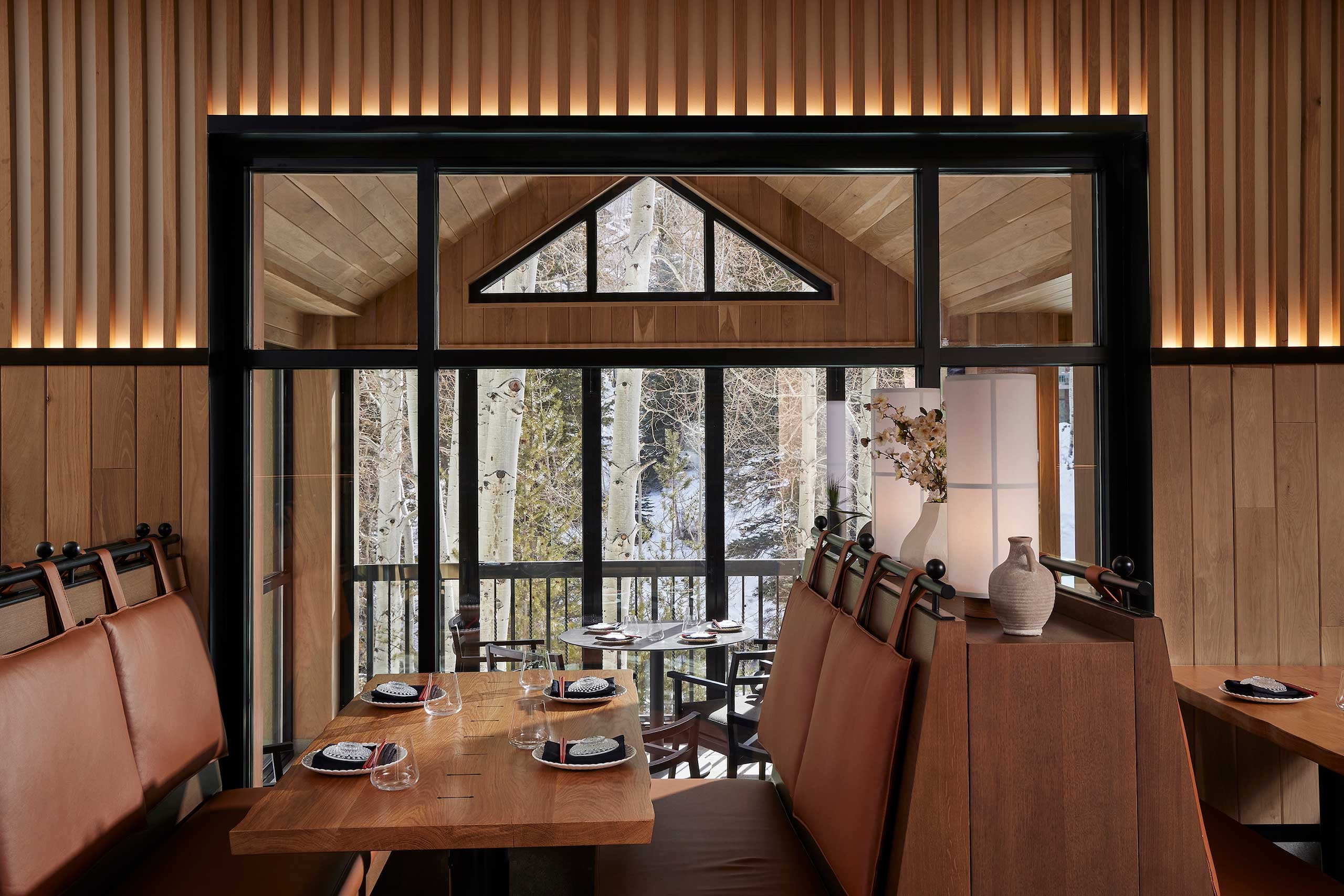 A cozy restaurant interior with wood-paneling and large windows overlooking snowy trees. Tables set with plates and glasses, warm and inviting atmosphere.
