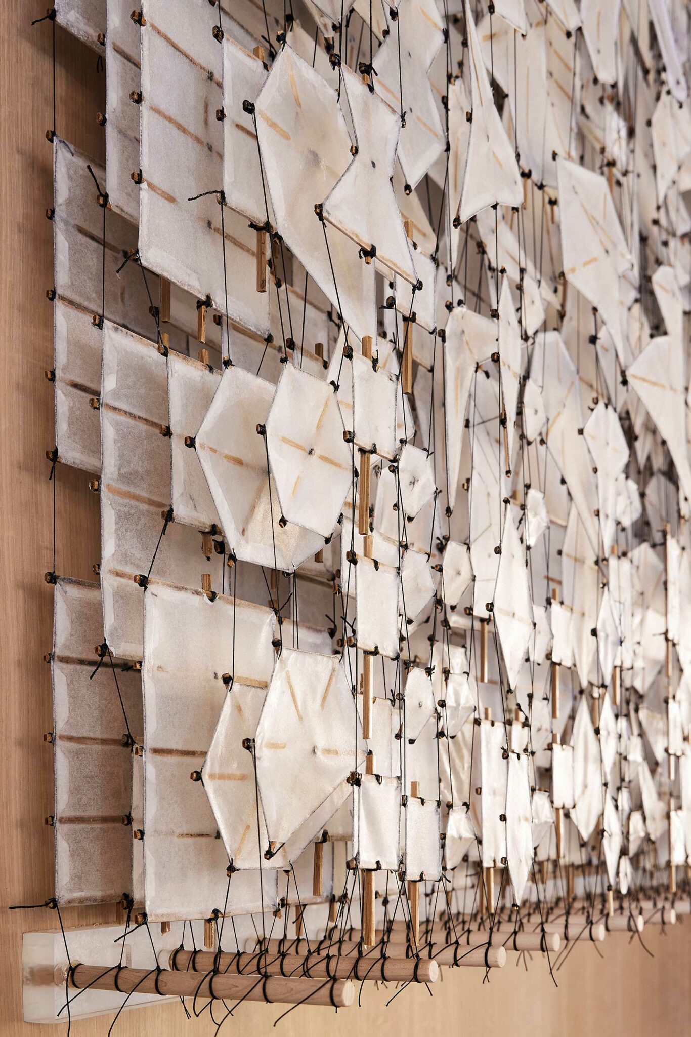 Intricate wall installation featuring white geometric fabric shapes attached with black strings and wooden pegs, creating a modern, textured pattern.