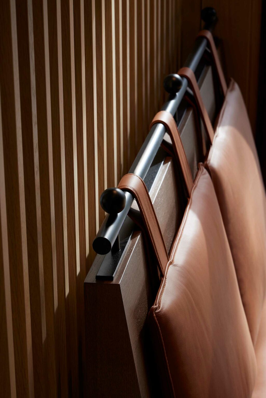 Elegant close-up of a wooden slat wall with a sleek black metal rail and brown leather straps. The soft light casts gentle shadows, conveying warmth.