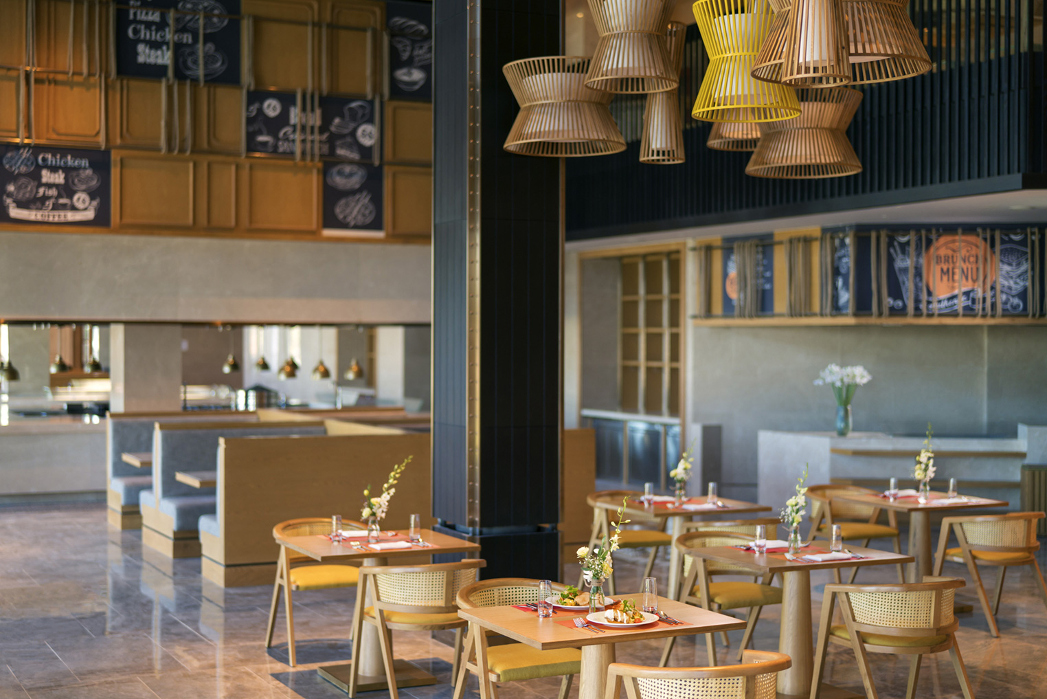 Modern restaurant interior with wooden tables and wicker chairs. Warm lighting from overhead woven lampshades creates an inviting and cozy atmosphere.
