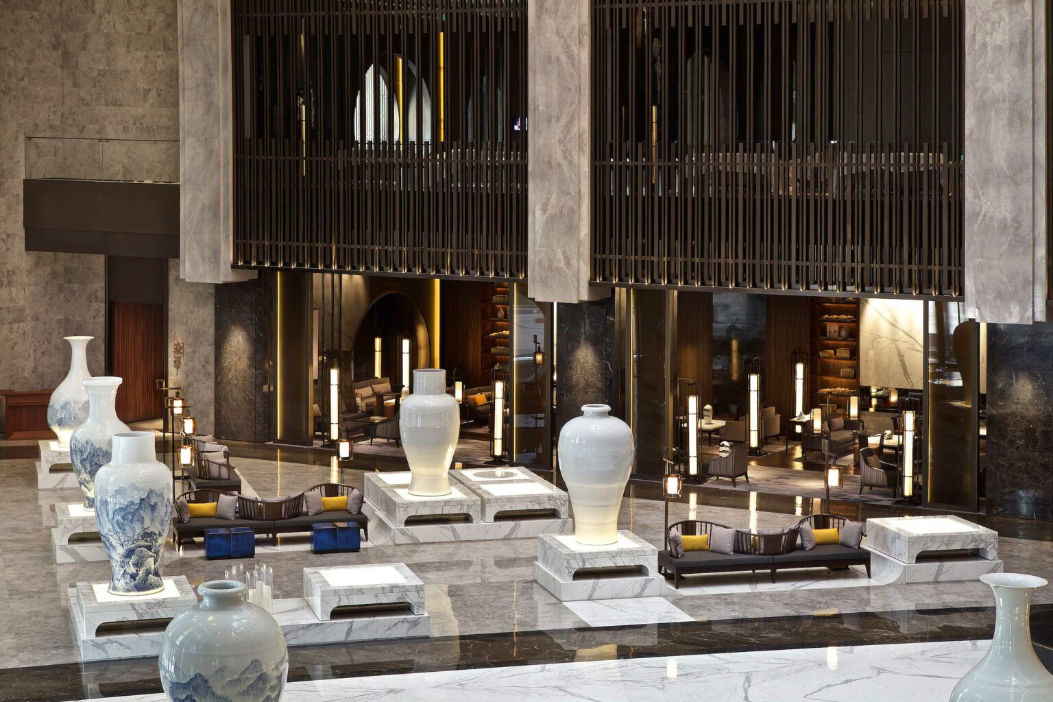 Luxurious hotel lobby with large white vases on marble bases, plush seating, and warm lighting. Modern, elegant design evokes a sophisticated atmosphere.