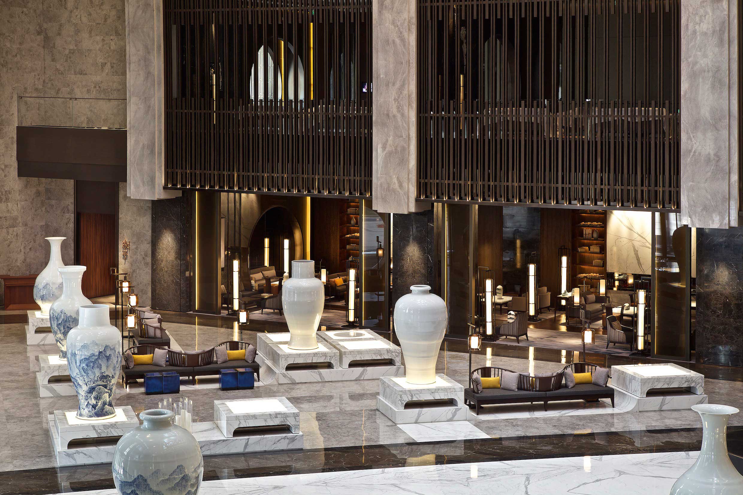 Luxurious hotel lobby with large white vases on marble bases, plush seating, and warm lighting. Modern, elegant design evokes a sophisticated atmosphere.