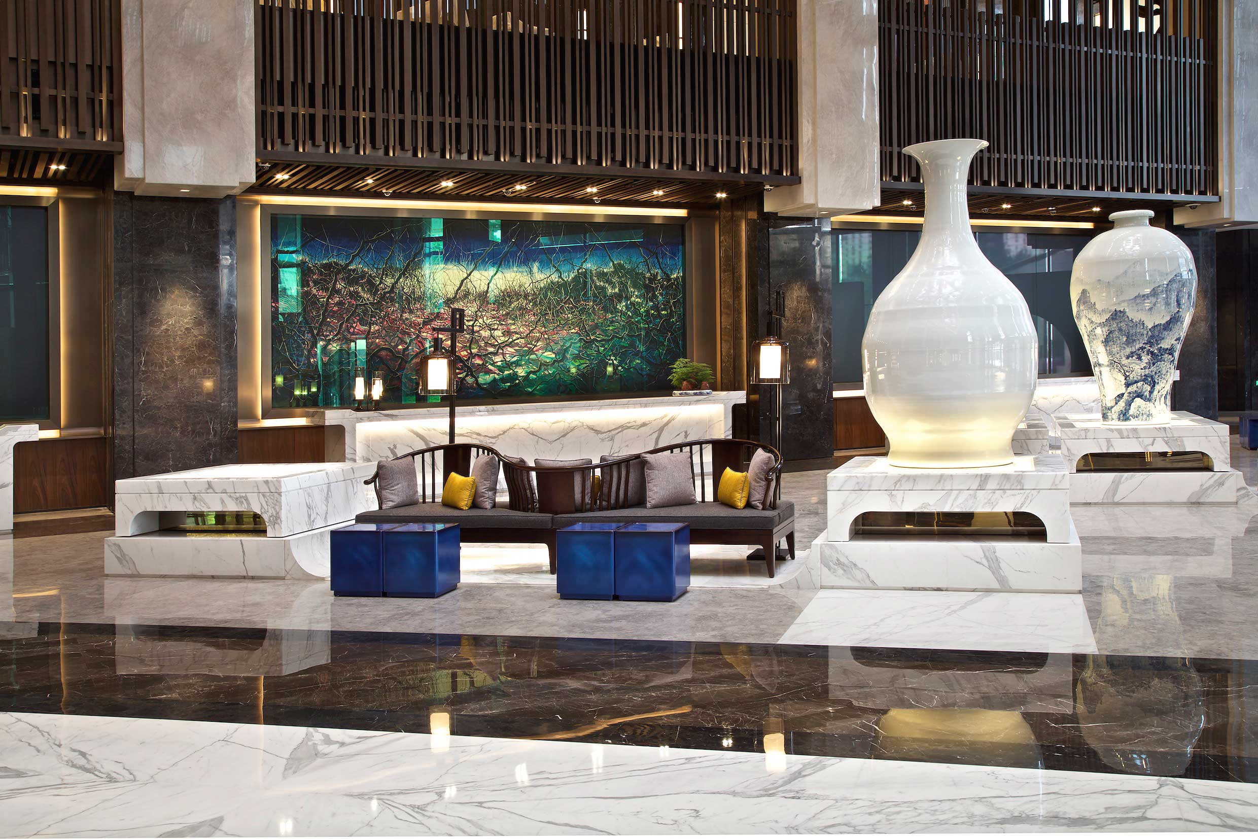 Luxurious hotel lobby with elegant marble decor, large ceramic vases, modern seating arrangement with cushions, and a vibrant abstract wall art.