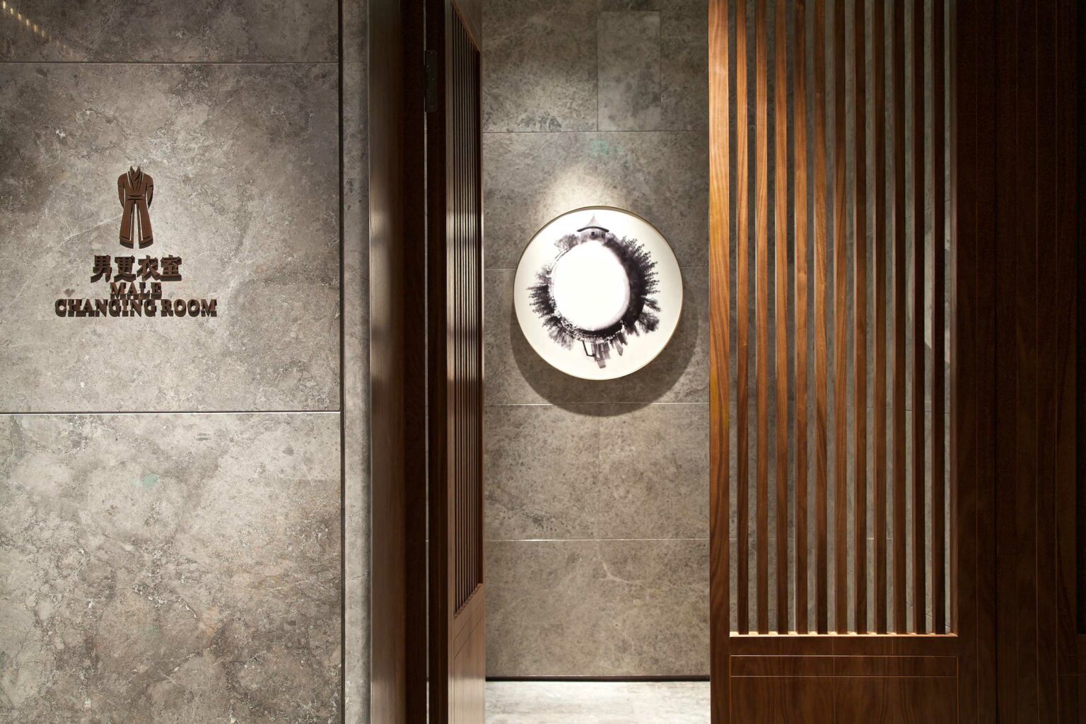 Men's changing room sign on a gray marble wall of a hotel spa. Adjacent is a modern art piece with black brush strokes, enhancing a sophisticated ambiance.