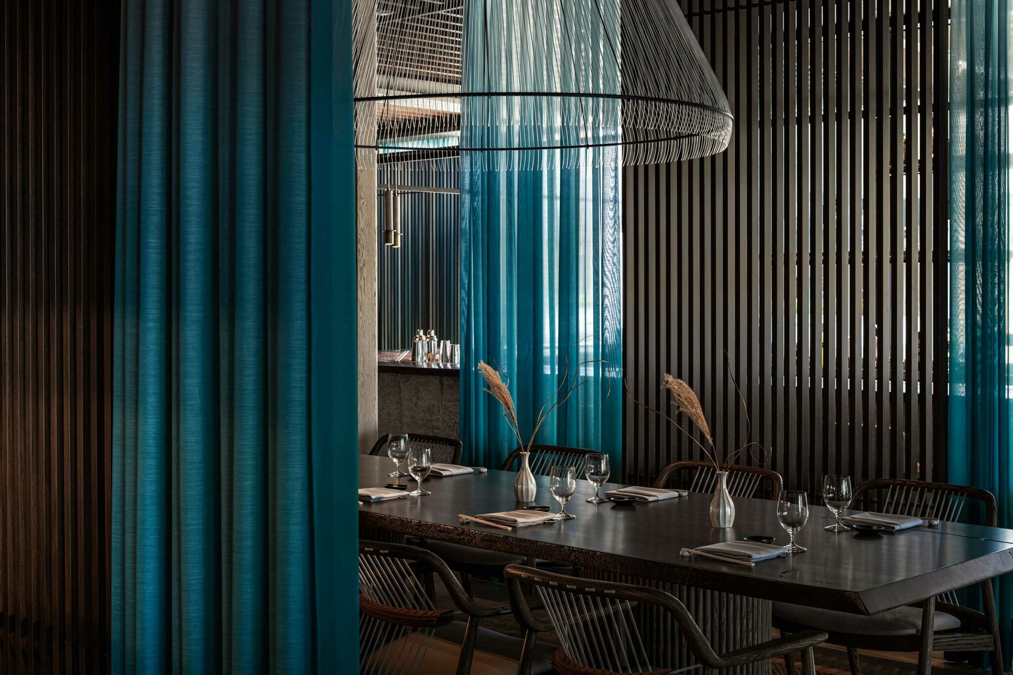 Sophisticated dining room with a dark wood table set for eight. Elegant blue curtains and sleek vertical slats create a modern, serene ambiance.