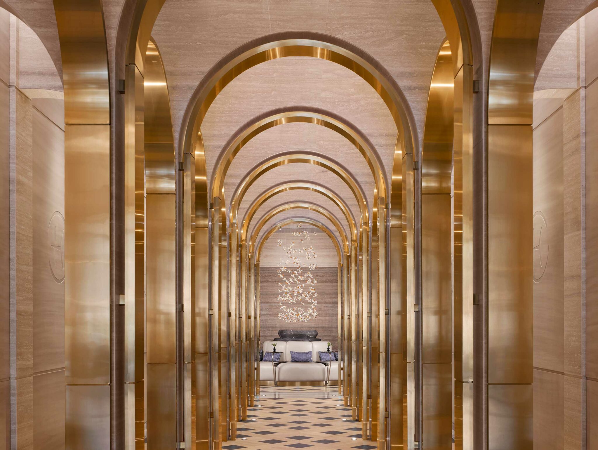 Luxurious resort spa hallway with golden arches receding into the distance, leading to a plush seating area. A sparkling chandelier adds elegance and warmth.