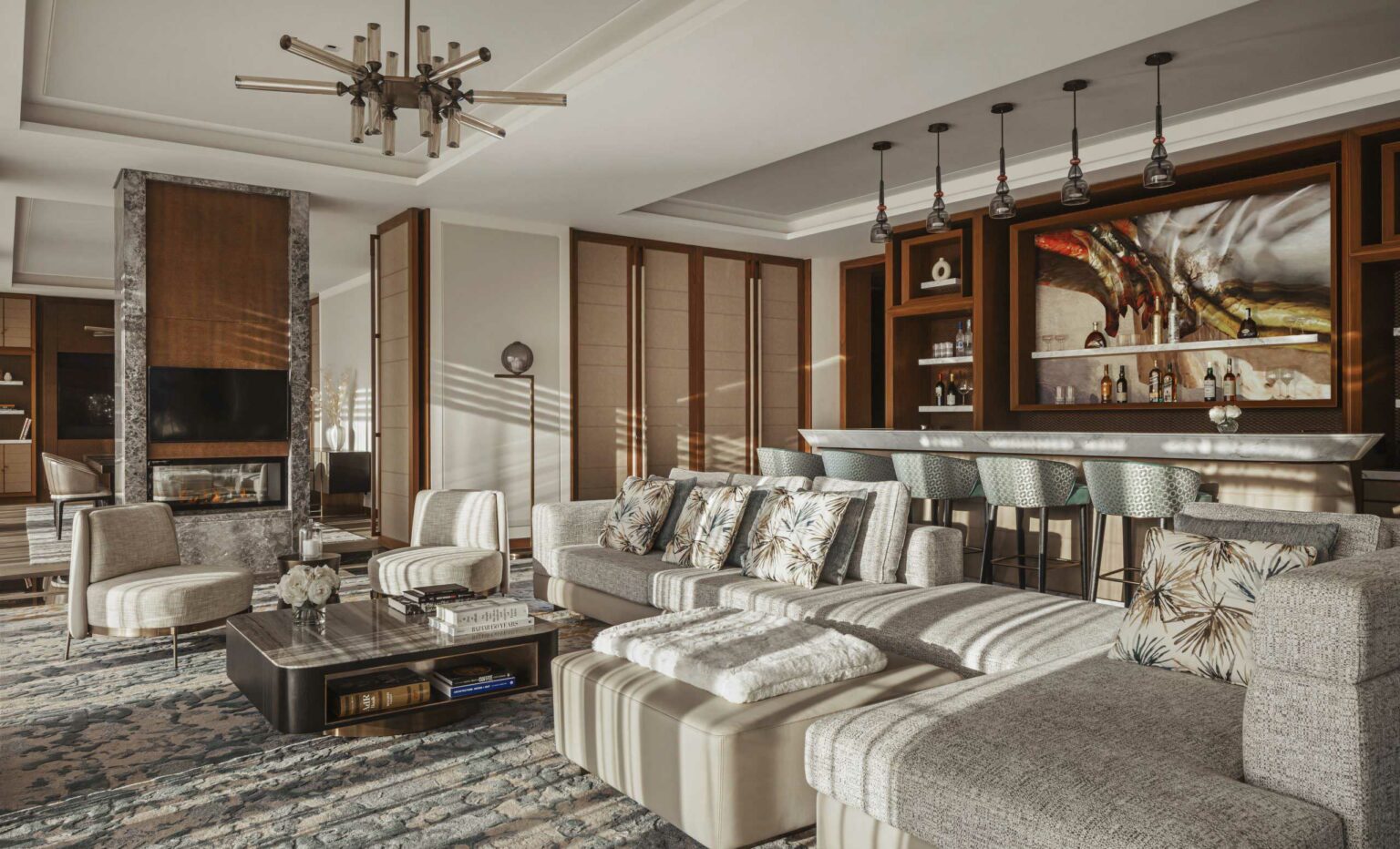 A modern, elegant resort lounge with a plush gray sectional sofa, floral cushions, a marble coffee table, a fireplace, and a stylish bar area. Warm lighting creates a cozy atmosphere.