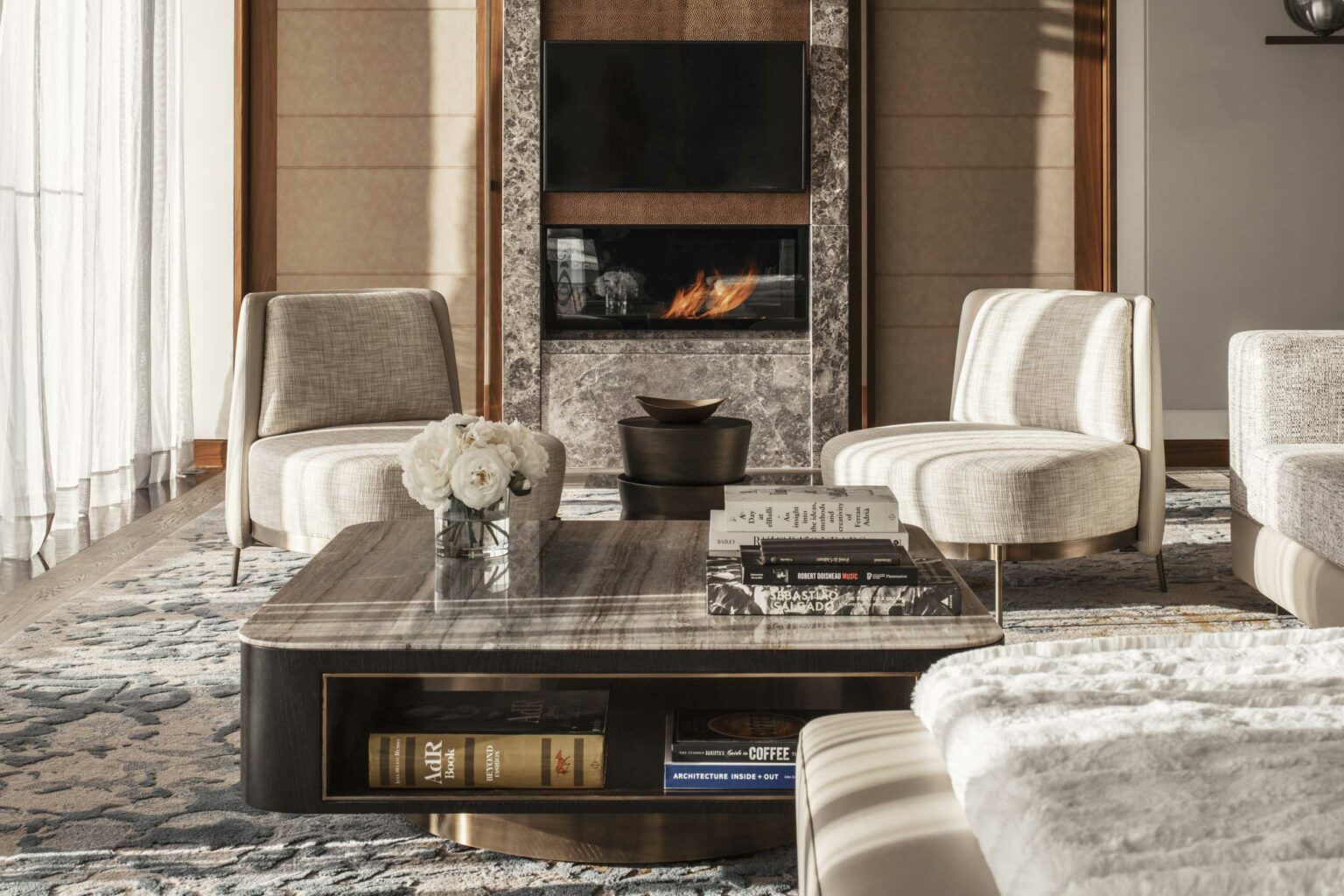 Luxurious resort lounge with a cozy fireplace, elegant marble coffee table, two modern beige chairs, and books and flowers adding a sophisticated touch.