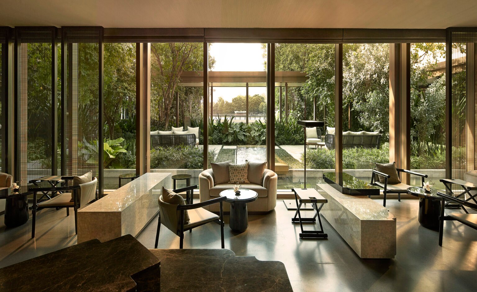 A modern hotel spa lounge with floor-to-ceiling windows overlooking a lush garden. Neutral-toned furniture creates a serene and inviting ambiance.