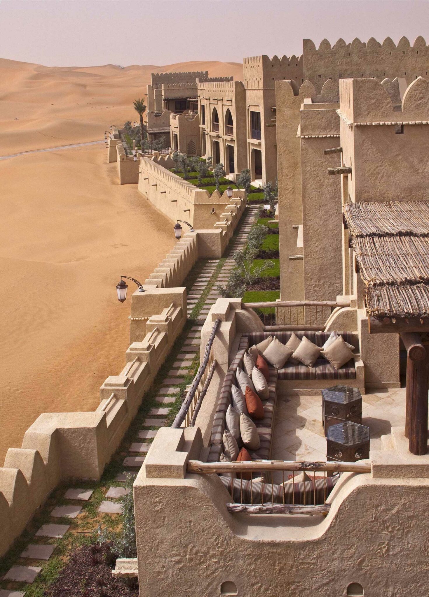 Luxury desert resort with stone buildings featuring arches and a cozy outdoor seating area. The setting is calm, with expansive sand dunes nearby.