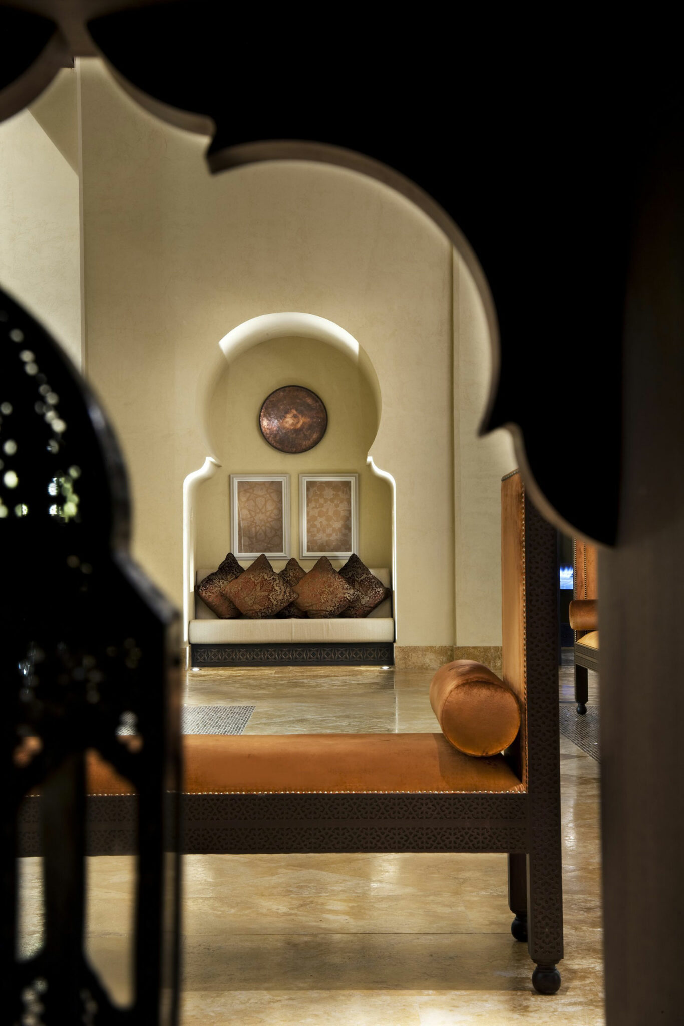 Cozy luxury resort interior with a Moroccan arch framing a seating alcove. Earth-toned cushions adorn the bench beneath a round wall art, exuding warmth and elegance.