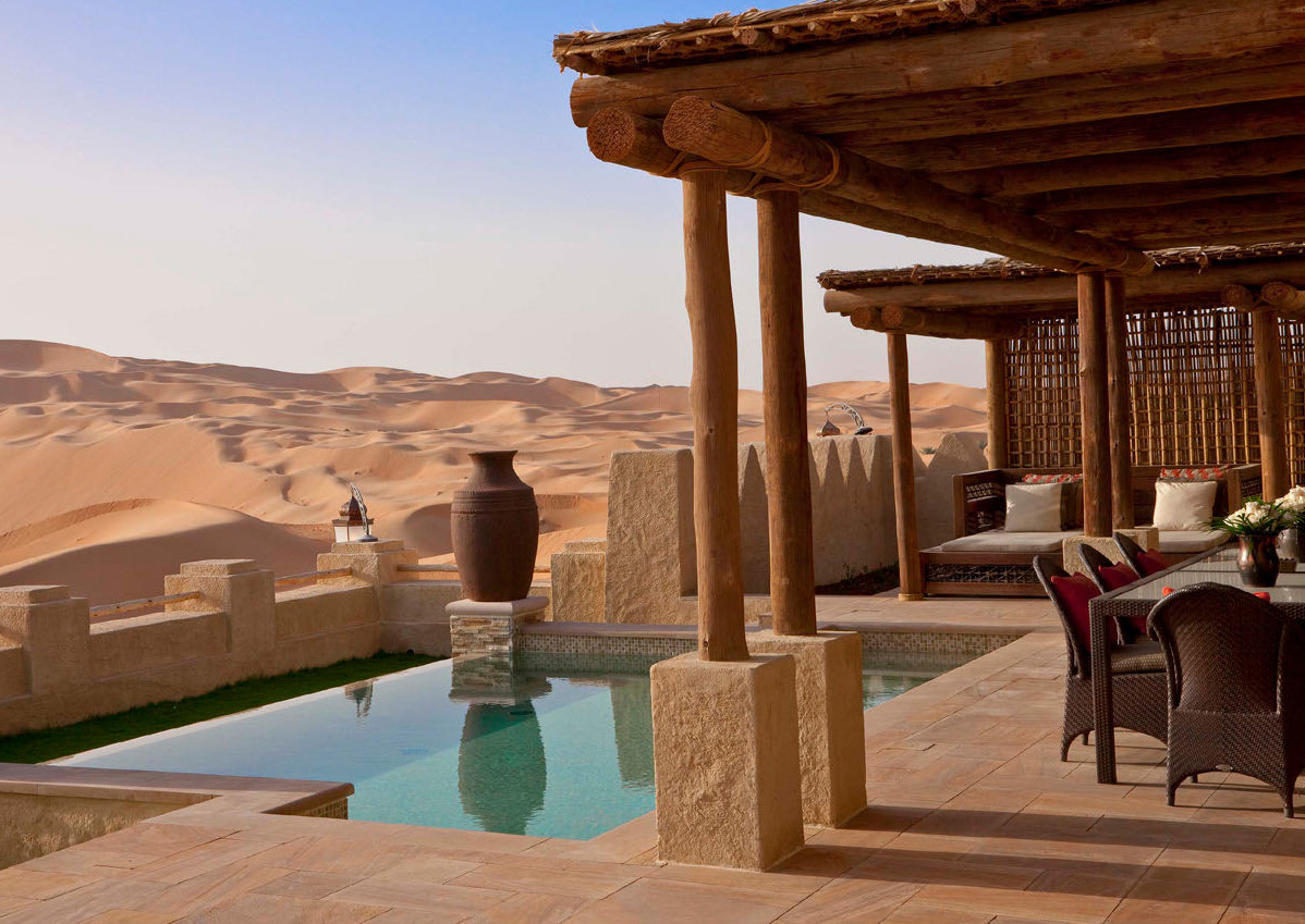 A luxurious desert resort with a pool overlooks vast sand dunes. Rustic wood and stone architecture create a serene, inviting atmosphere.