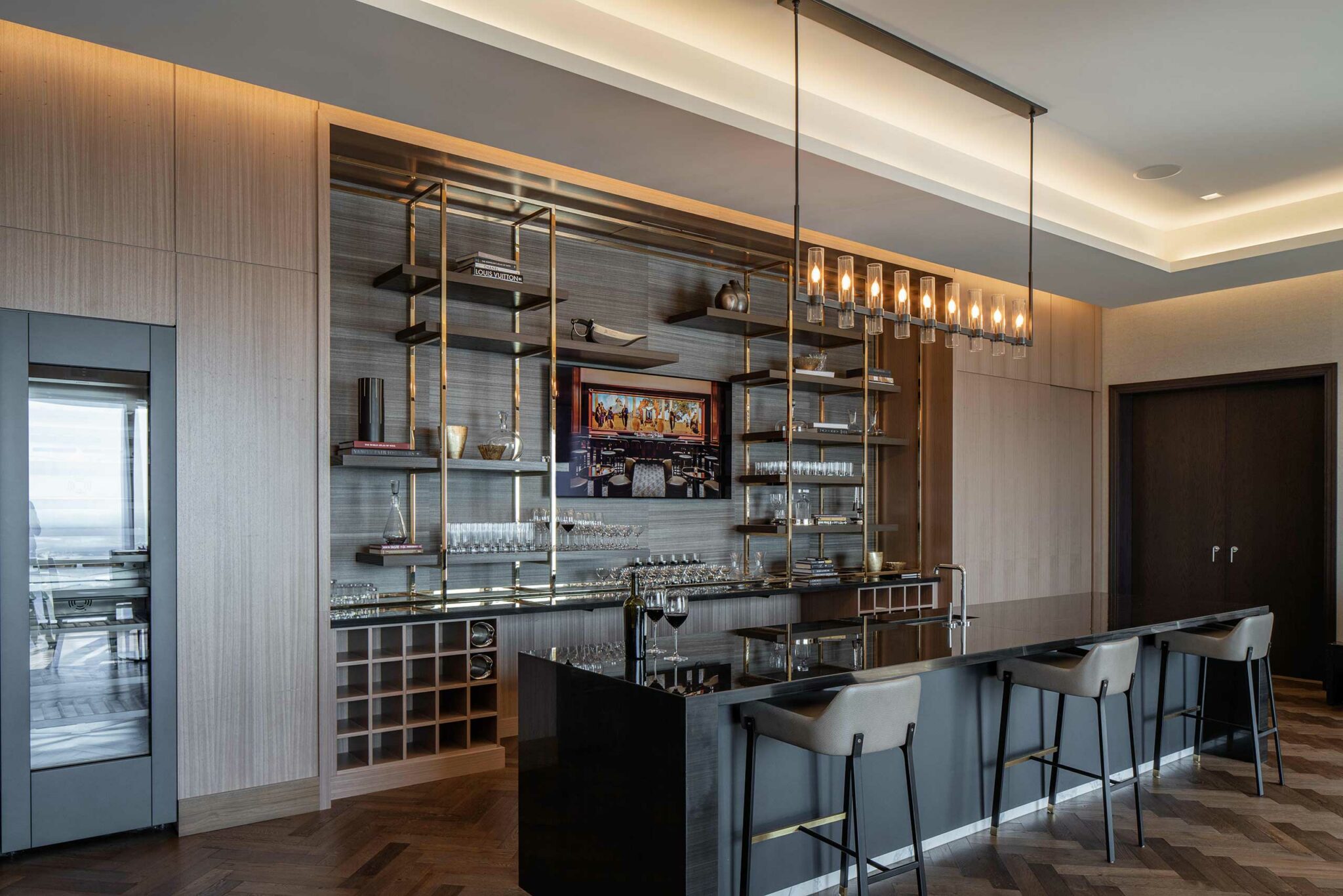 Modern home bar with sleek black counter, high-backed stools, and a glass rack. Elegant cabinetry, warm lighting, and art create a sophisticated ambiance.