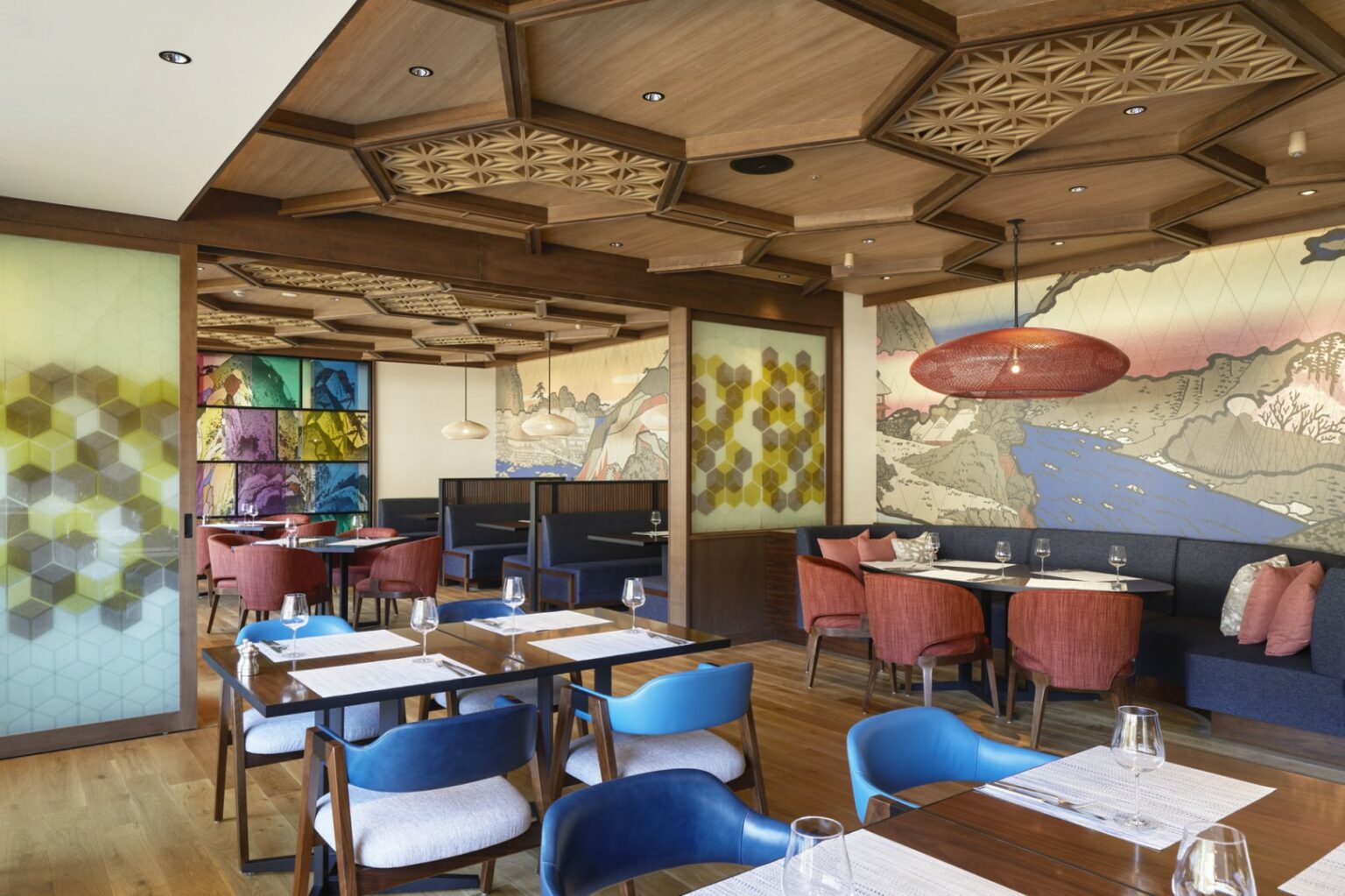 Modern restaurant interior with wooden ceilings and hexagonal accents. Vibrant colored chairs, mural of landscapes, and soft lighting create a cozy atmosphere.