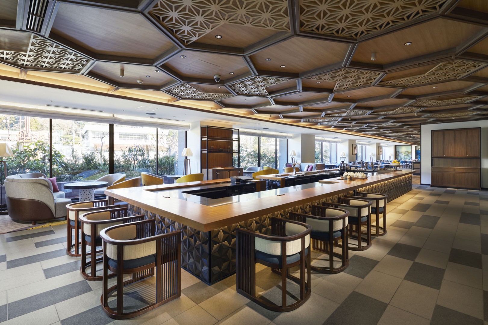 Modern restaurant lounge with geometric wooden ceiling, large windows, and sleek seating around a central table. Bright, inviting atmosphere with natural light.