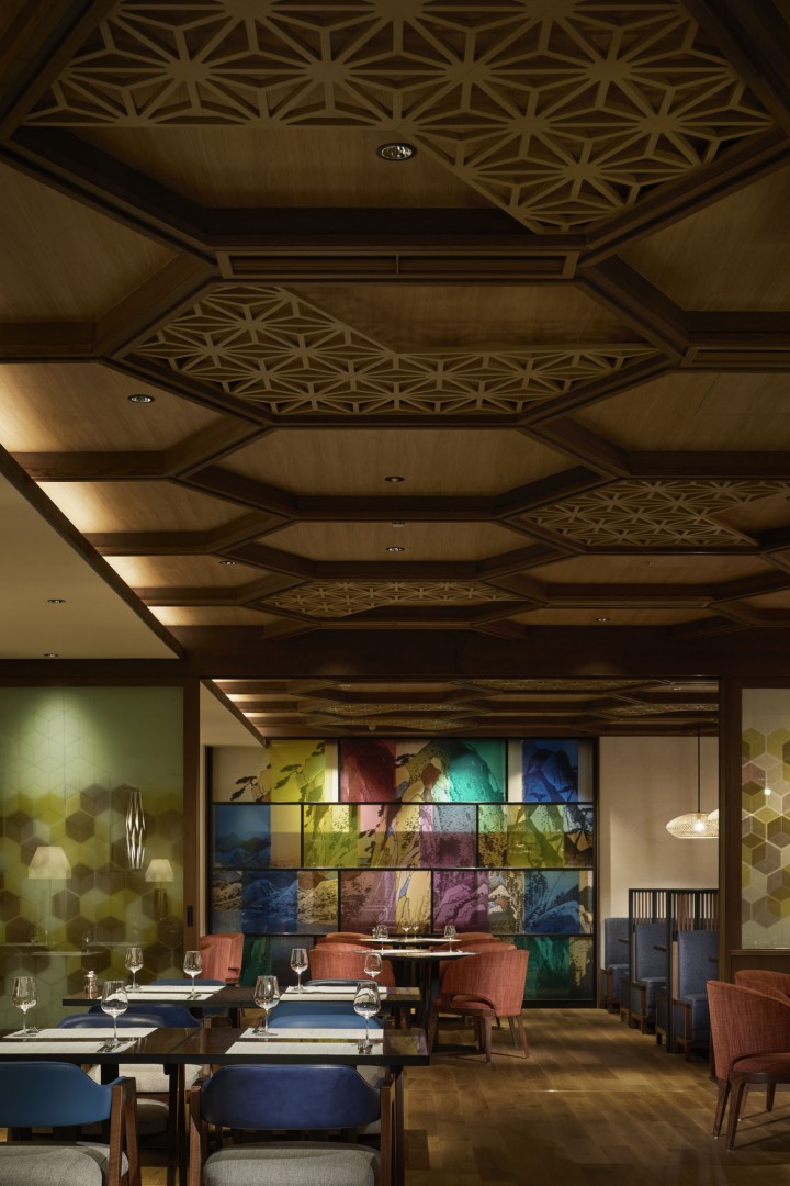 Sophisticated restaurant interior with geometric wooden ceiling, colorful abstract wall art, and elegant table settings. Warm, inviting atmosphere.