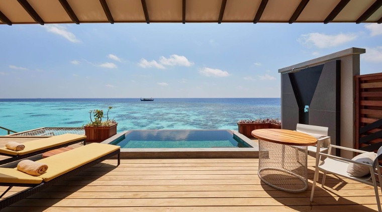 Private beachfront hotel deck with a small pool overlooking a serene, crystal-clear ocean. Two lounge chairs and a round table create a tranquil, inviting setting.