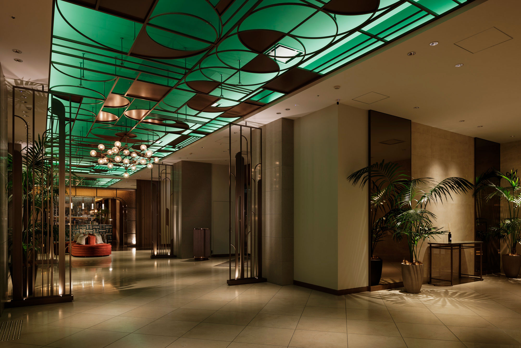 Stylish hotel lobby with an artistic green ceiling and warm lighting. Features modern decor, potted plants, and a cozy seating area, creating a welcoming ambiance.