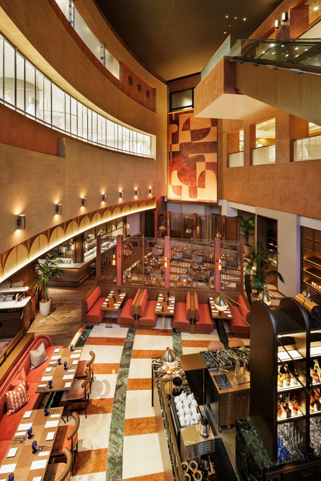 Spacious restaurant interior with warm lighting, red booths, and elegant decor. Features a high ceiling, abstract wall art, and arranged dining tables.