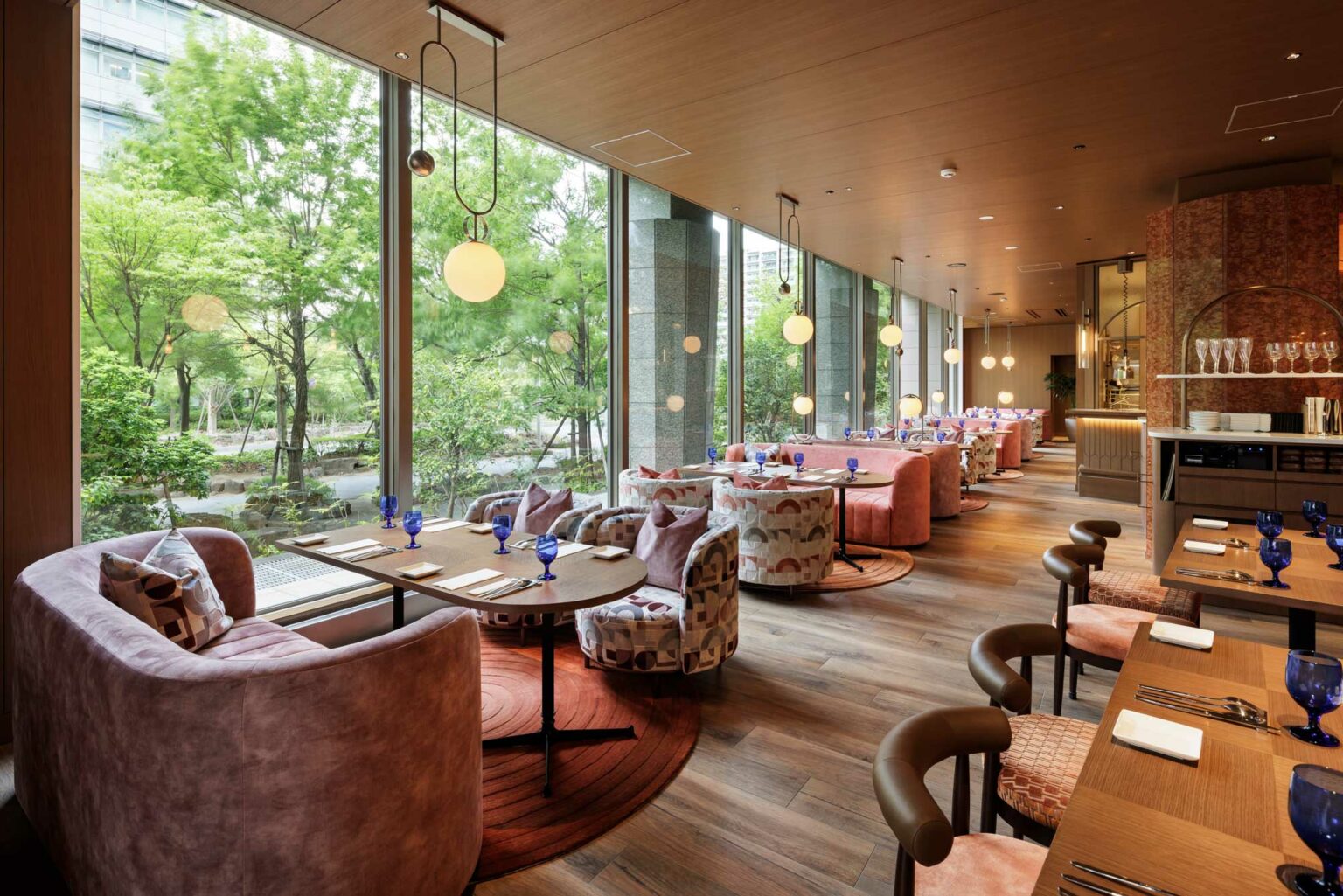 Chic restaurant with large windows, plush seating, and elegant wooden floors. Soft lighting and nature views create a calm, inviting atmosphere.