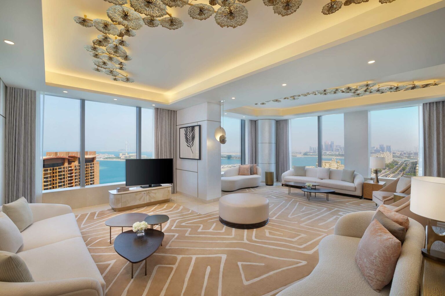 Luxurious suite living room with modern decor features elegant furniture, abstract ceiling art, and large windows offering a stunning ocean and city view.