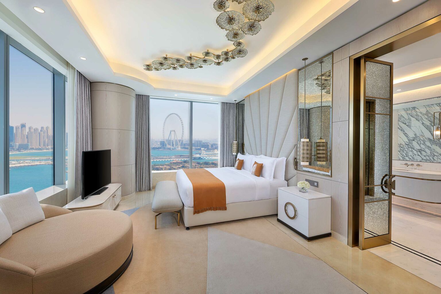 Luxurious hotel room with a large window view of a city skyline and Ferris wheel. Elegant decor includes a plush bed, neutral tones, and gold accents.