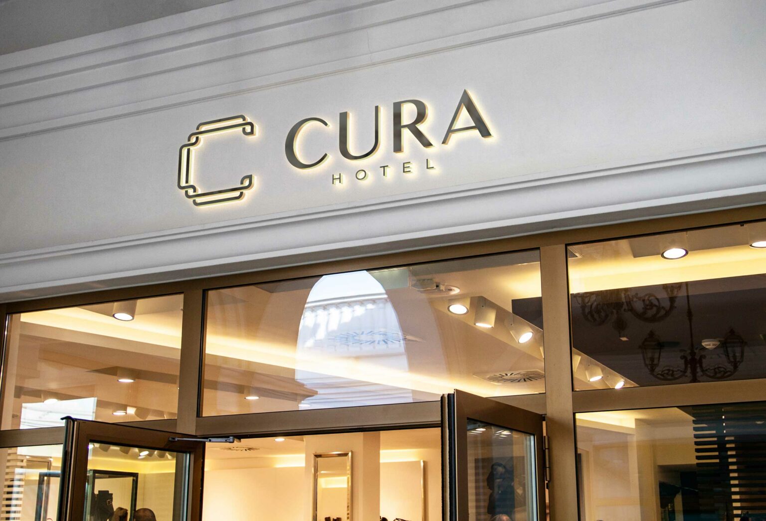 Entrance of CURA Hotel featuring illuminated modern signage and a glass door entrance, conveying a welcoming and upscale atmosphere.