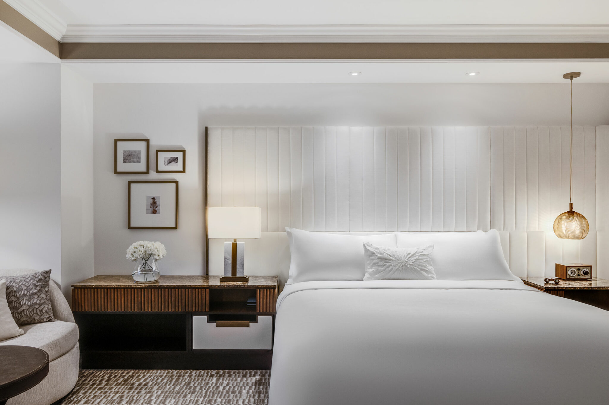 Elegant suite bedroom with a plush white bed, light wood nightstands, modern lamps, and framed art. Soft, neutral tones create a calm, inviting atmosphere.