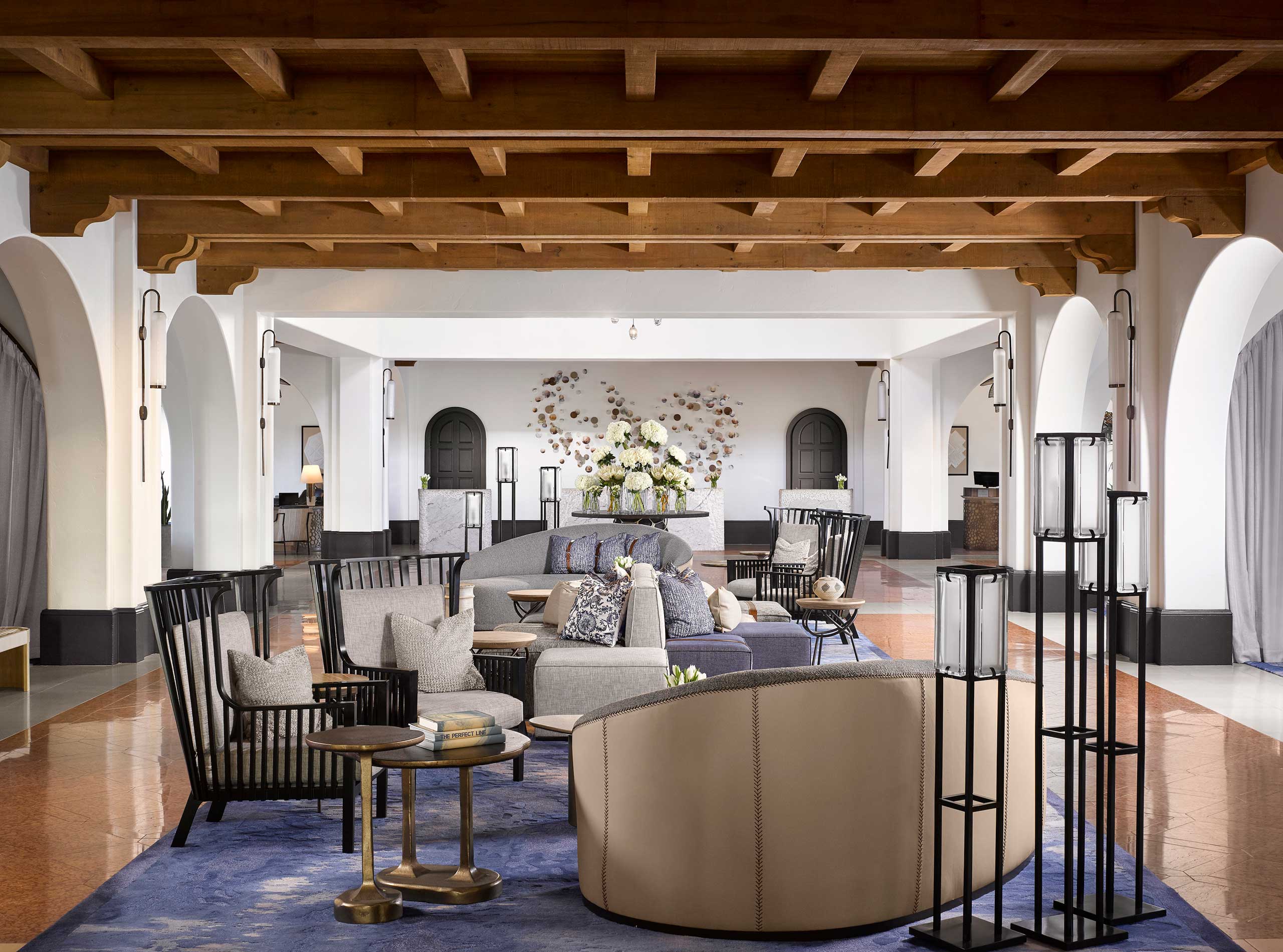Spacious hotel lobby with elegant, modern furnishings including plush sofas, armchairs, and a floral centerpiece. Warm tones and soft lighting create a welcoming atmosphere.