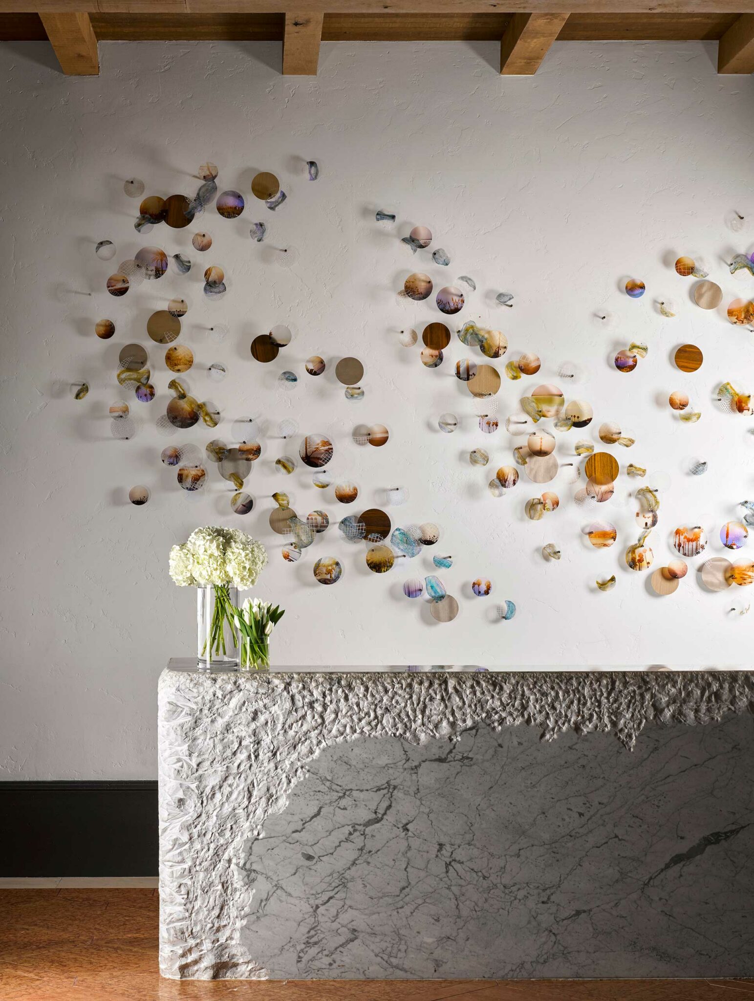 Artistic wall design with colorful, textured circles seemingly floating. A textured stone counter with white flowers adds elegance and contrast within a hotel setting.