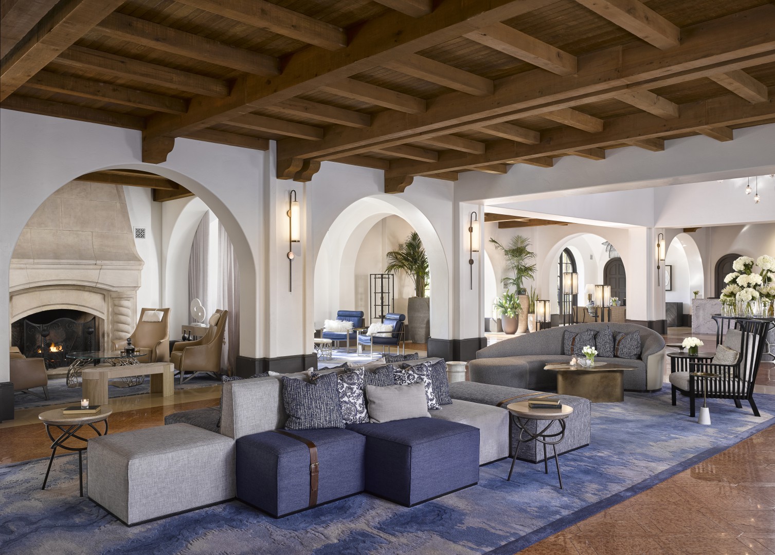 Luxurious hotel lounge featuring cozy seating with blue and gray cushions, warm lighting, a fireplace, and elegant arches creating a welcoming ambiance.