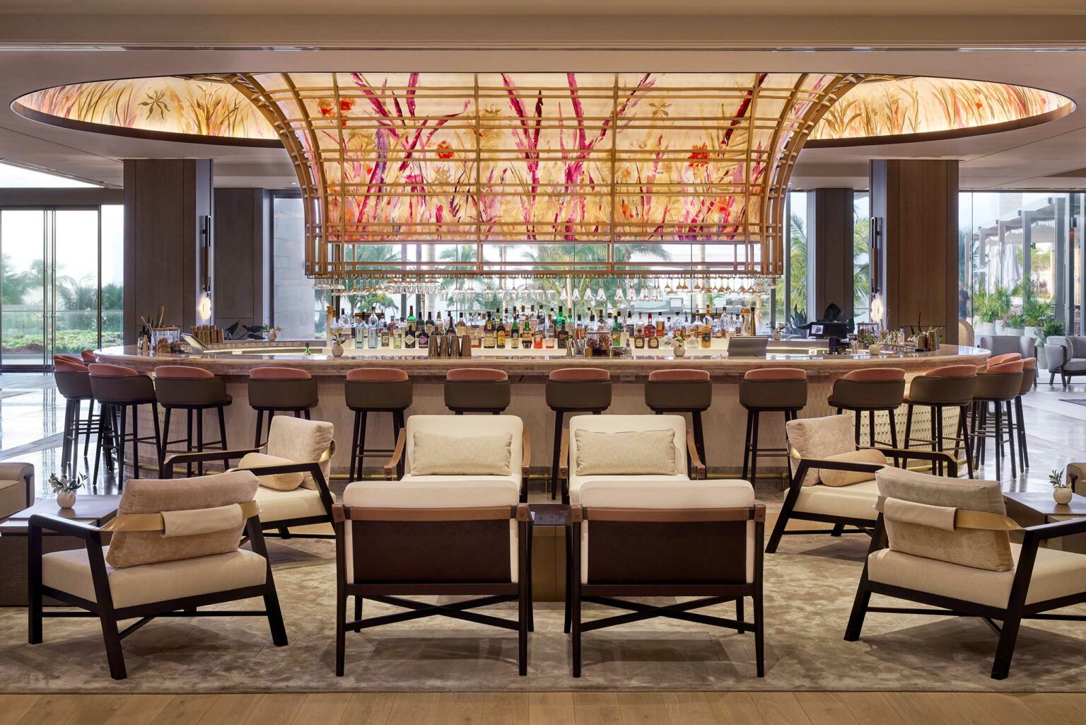 Luxurious hotel bar interior featuring a large, illuminated floral ceiling, surrounded by plush chairs and stools, creating a welcoming and elegant ambiance